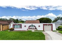 Unique home featuring a white facade, red trim, an attached garage, and a well-maintained green lawn at 3526 Overland Dr, Holiday, FL 34691