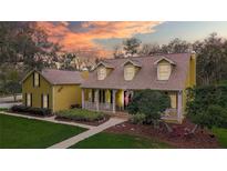 Charming two-story yellow home with a welcoming front porch and meticulously landscaped front yard at 1031 Pomme De Pin Ln, New Port Richey, FL 34655