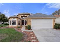 Charming tan home featuring a two-car garage, landscaped front yard, and double-door front entrance at 150 Center Oak Cir, Spring Hill, FL 34609