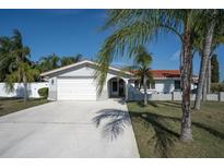Charming home featuring a white exterior, well-manicured lawn, and a spacious driveway, complemented by tropical palm trees at 5061 Ensign Loop, New Port Richey, FL 34652