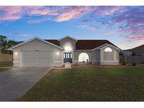 Charming single Gathering home features a 2-car garage and well-maintained lawn under a beautiful sunset sky at 3606 Dow Ln, Spring Hill, FL 34609