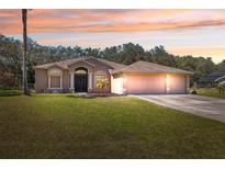 Charming single-story home with a three-car garage and a well-manicured lawn under a beautiful sunset sky at 18251 East Rd, Hudson, FL 34667