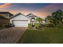 Beautiful single-Gathering home with lush landscaping, brick driveway, and two-car garage at sunset at 215 Arbor Woods Cir, Oldsmar, FL 34677