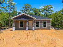 Charming single-story home featuring neutral siding, gray accents and a covered front porch in a sunny, wooded setting at 18082 Parakeet Rd, Brooksville, FL 34614