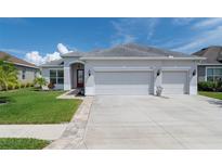 Charming single-story home with a well-manicured lawn, three-car garage, and inviting red front door at 14604 Strathglass Dr, Hudson, FL 34667
