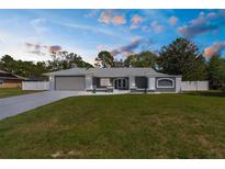 Charming single-story home with a well-manicured lawn, gray exterior, and an attached two-car garage at dusk at 1156 Battersea Ave, Spring Hill, FL 34609