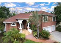 Beautiful two-story red brick home featuring a well-manicured lawn and colorful landscaping at 1218 Castle Ter, Tarpon Springs, FL 34689