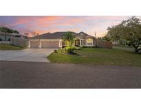 Charming single-story home with a three-car garage and well-manicured lawn at sunset at 12300 Drake Ln, Spring Hill, FL 34609