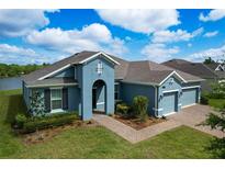 Beautiful single-story home with a three-car garage, blue exterior paint, and a well-maintained lawn at 19879 Tattnall Way, Brooksville, FL 34601