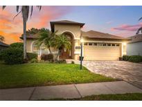 Charming single-story home with lush landscaping, paver driveway, and a two-car garage at sunset at 11631 Wayside Willow Ct, Hudson, FL 34667