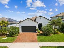 Charming single-story home featuring a brick driveway, lush landscaping, and a welcoming black garage door at 6229 Sea Air Dr, Apollo Beach, FL 33572
