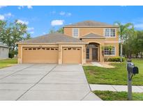Inviting tan two-story home featuring a well-manicured lawn, three-car garage, and charming front-yard landscaping at 4335 Canongate Ct, Spring Hill, FL 34609