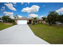 Charming single-story home with a well-manicured lawn, a long driveway, and lush landscaping under a blue sky at 13100 Fish Cove Dr, Spring Hill, FL 34609