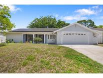 Charming single-story home with a two-car garage, well-maintained lawn, and solar panels on the roof at 12204 Pepper Mill Dr, Hudson, FL 34667
