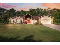 Charming single-story home showcasing a well-manicured lawn and inviting red double-door entry at 4469 Lake In The Woods Dr, Spring Hill, FL 34607