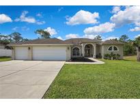 Charming single-story home with a three-car garage, arched entryway, and well-maintained lawn at 11336 Flower Ave, Weeki Wachee, FL 34613