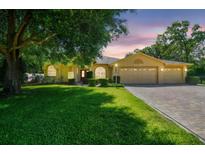 Inviting single-story home with a three-car garage, well-manicured lawn, and a paver driveway at 18502 Winding Oaks Blvd, Hudson, FL 34667
