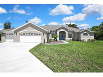 Inviting one-story home featuring a well-manicured lawn and a three-car garage with white doors at 7495 Birdland Cres, Spring Hill, FL 34607