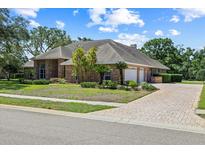 Lovely home featuring a three car garage, brick exterior, and well-manicured landscaping at 888 Royal Birkdale Dr, Tarpon Springs, FL 34688
