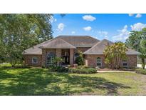 Charming brick home featuring arched windows, lush landscaping, and a well-maintained lawn on a sunny day at 888 Royal Birkdale Dr, Tarpon Springs, FL 34688
