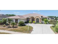 Charming single-story home featuring an arched entryway, lush landscaping, and a spacious driveway on a sunny day at 1420 Winding Willow Dr, Trinity, FL 34655