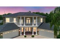 Elegant two-story home featuring white columns, a balcony, a dark roof, and a three-car garage at 15906 Prince William Pl, Odessa, FL 33556