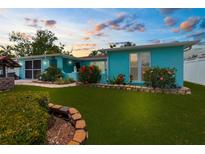 Charming turquoise home with a lush green lawn and vibrant flowerbeds beneath a colorful sky at 9015 Mark Twain Ln, Port Richey, FL 34668