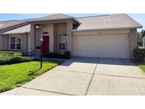 Inviting single-story home featuring a red front door, two-car garage, and well-maintained front yard at 18418 Bent Pine Dr, Hudson, FL 34667