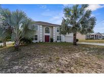 Charming two-story home featuring a red front door, a manicured lawn, and beautiful palm trees at 6440 Curtiss Ln, Spring Hill, FL 34609