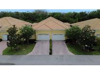 Charming two-unit villa featuring a yellow exterior, tile roof, and brick-paved driveway leading to attached garages at 4837 Rainbow Race, New Port Richey, FL 34652