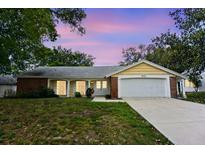 Charming single-story home with a well-manicured lawn, two-car garage and beautiful landscaping at sunset at 12411 Yorktown Ln, Hudson, FL 34667