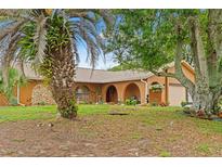 Inviting single-story home featuring a meticulously manicured lawn, mature trees, and an arched entryway at 4190 Lema Dr, Spring Hill, FL 34609