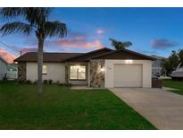 Charming single-story home featuring a well-maintained lawn and a classic stone facade detail at sunset at 7520 Mako Dr, Hudson, FL 34667