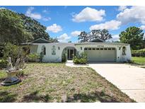 An exterior view of the home featuring a two-car garage, arched entry, and lush greenery at 12722 Oak Tree Dr, Hudson, FL 34667