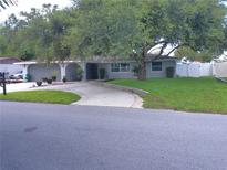 Charming single-story home featuring a well-maintained lawn, mature trees, and a curved driveway leading to a two-car garage at 3207 Jarvis St, Holiday, FL 34690