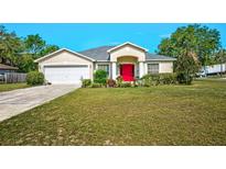 Charming home featuring a well-manicured lawn, colorful garden, and a striking red front door at 13317 Pinellas Ave, Spring Hill, FL 34609
