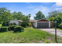 Charming single-Gathering home featuring a two-car garage and neutral stucco exterior, nestled amidst mature trees at 2443 Glenridge Dr, Spring Hill, FL 34609