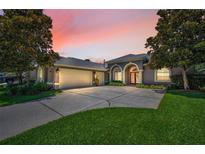 Charming gray home featuring a spacious driveway, two-car garage, arched entry, and mature landscaping at 4485 Gevalia Dr, Brooksville, FL 34604