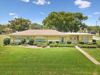 Charming yellow brick home with a well-manicured front lawn and lush, mature landscaping at 6823 Oak Hill Dr, New Port Richey, FL 34653