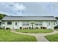 Charming, light-green two-unit condo with manicured lawn, flowerbeds, and sidewalk approach under a cloudy sky at 11619 Boynton Ln, New Port Richey, FL 34654