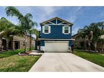 Two-story blue home featuring a large two-car garage, well-manicured lawn, and beautiful palm trees at 14008 Lugano Ct, Hudson, FL 34669