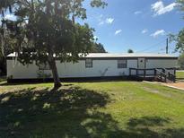 Exterior view of a single-story home featuring a well-maintained lawn, mature trees and wooden deck at 9444 Loras St, New Port Richey, FL 34654