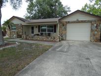 Charming home with a rock facade, attached garage, and inviting front porch with chairs and table at 7421 Fairfax Dr, Port Richey, FL 34668