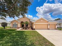 Beautiful, tan-colored single-story home with a three-car garage and a well-manicured lawn at 13248 Linzia Ln, Spring Hill, FL 34609