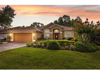 Inviting single-story home boasts a manicured lawn and vibrant landscaping, complemented by a brick driveway and a warm-toned facade at 19418 Morden Blush Dr, Lutz, FL 33558