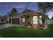 Charming single-story home with a well-manicured lawn, mature landscaping, and a two-car garage under a picturesque evening sky at 1862 Wood Bend St, Tarpon Springs, FL 34689