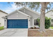 Charming single-story home featuring a blue garage door, gray stucco, and manicured landscaping at 8335 Crescent Moon Dr, New Port Richey, FL 34655