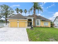 Charming yellow home with a two-car garage, brick driveway, manicured lawn, and mature palm trees at 5440 Manatee Point Drive, New Port Richey, FL 34652