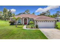 Charming home showcasing a well-manicured lawn, complemented by a red front door and a two-car garage at 12323 House Finch, Weeki Wachee, FL 34614