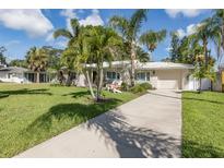 Charming single-story home with a well-manicured lawn, palm trees, and a driveway leading to an attached garage at 1830 Santa Barbara Dr, Dunedin, FL 34698